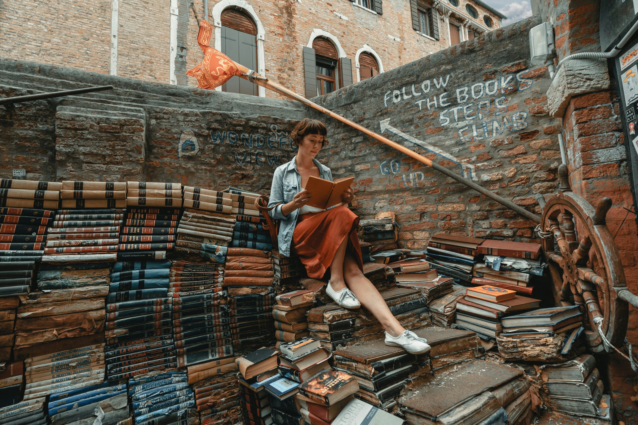 Woman sitting on top of a pile of books reading